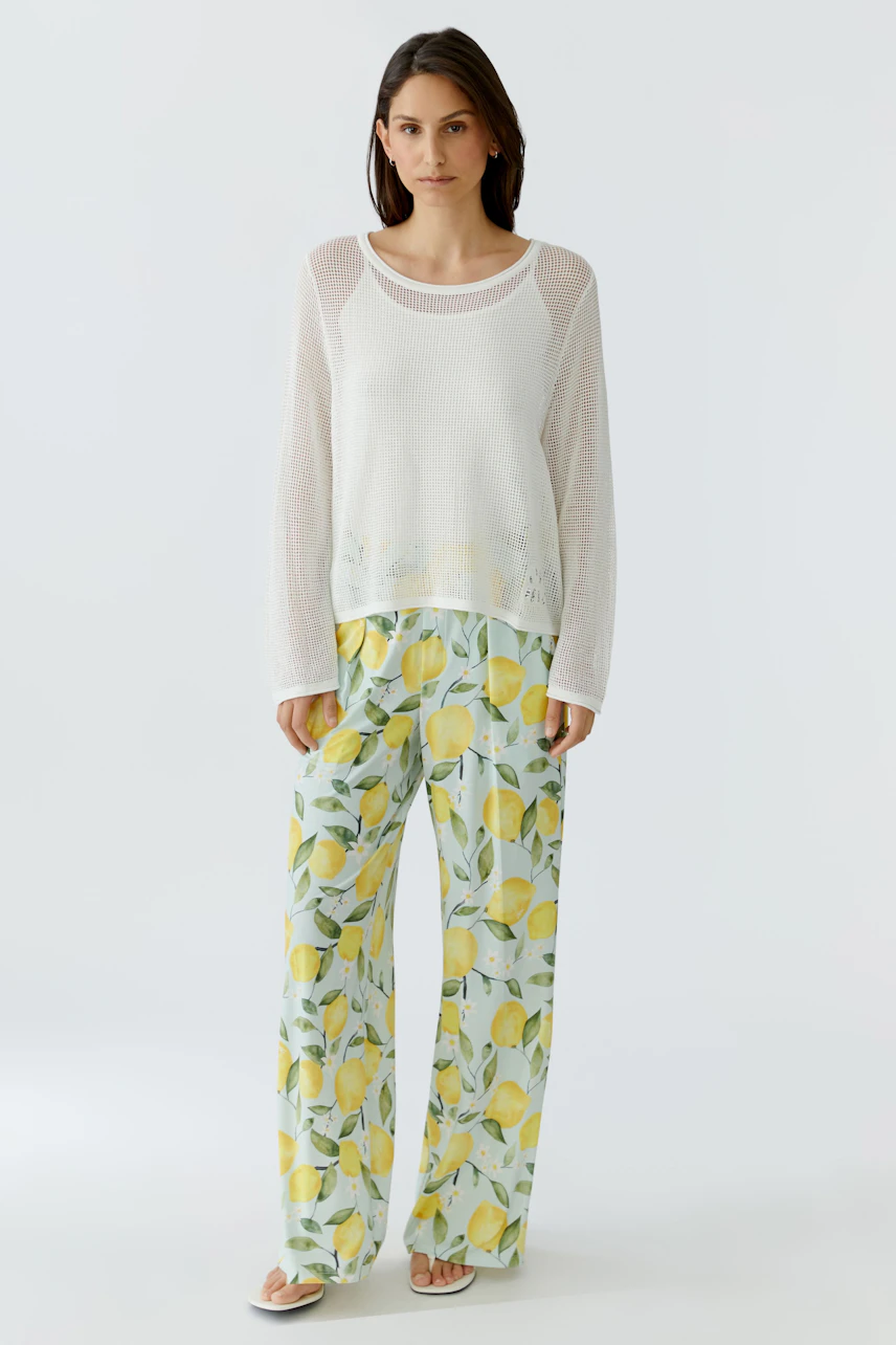 Lässiger Damen-Pullover: Frau im weißen Pullover mit transparenten Ärmeln und bunter Hose mit Zitronenmuster.