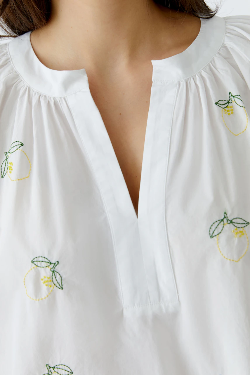 Weiße Tunika mit Zitronenstickerei: Frau trägt luftige Tunika mit V-Ausschnitt, ideal für sommerliche Tage.