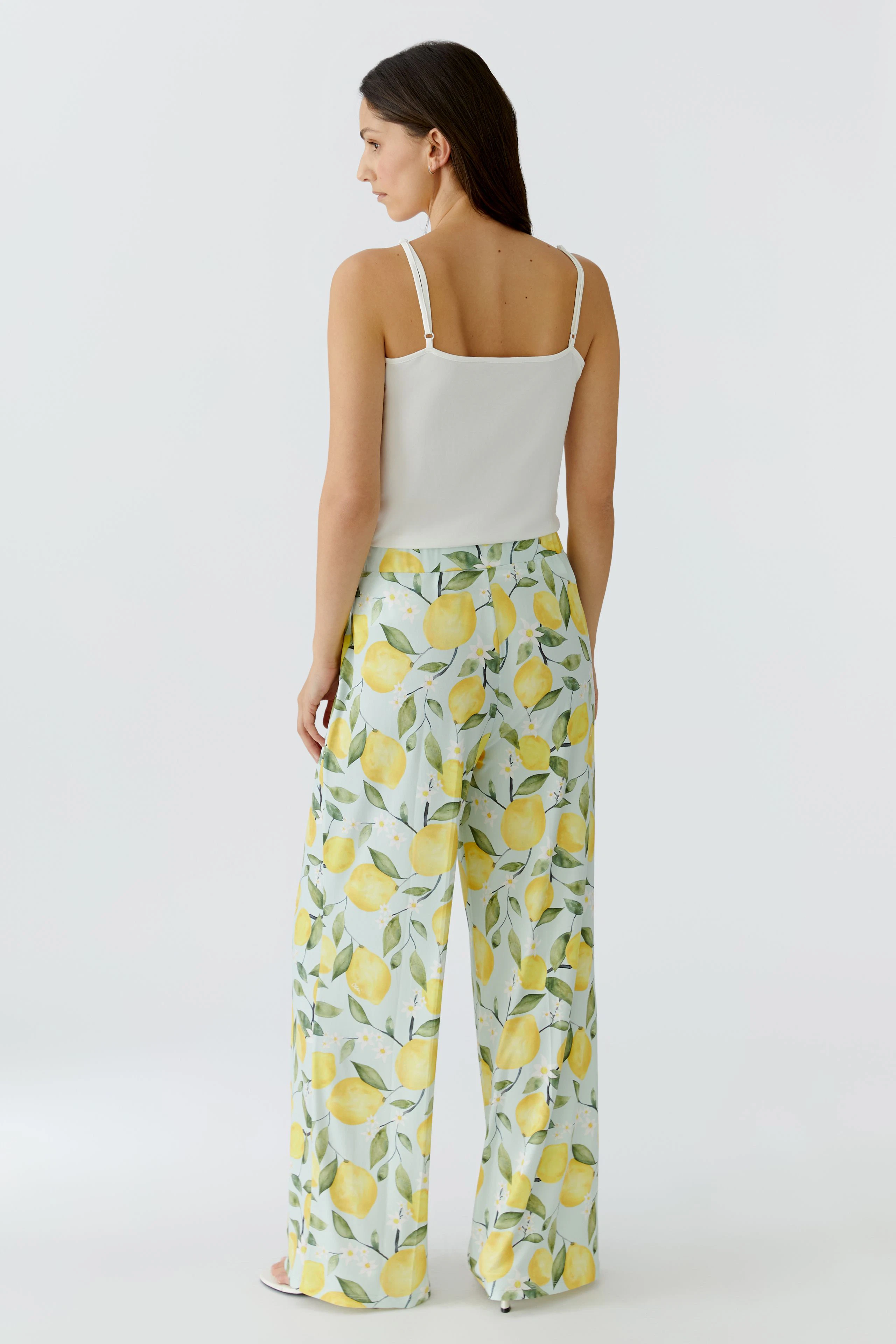 Woman in lemon-patterned pants and white top, showcasing vibrant, casual style.