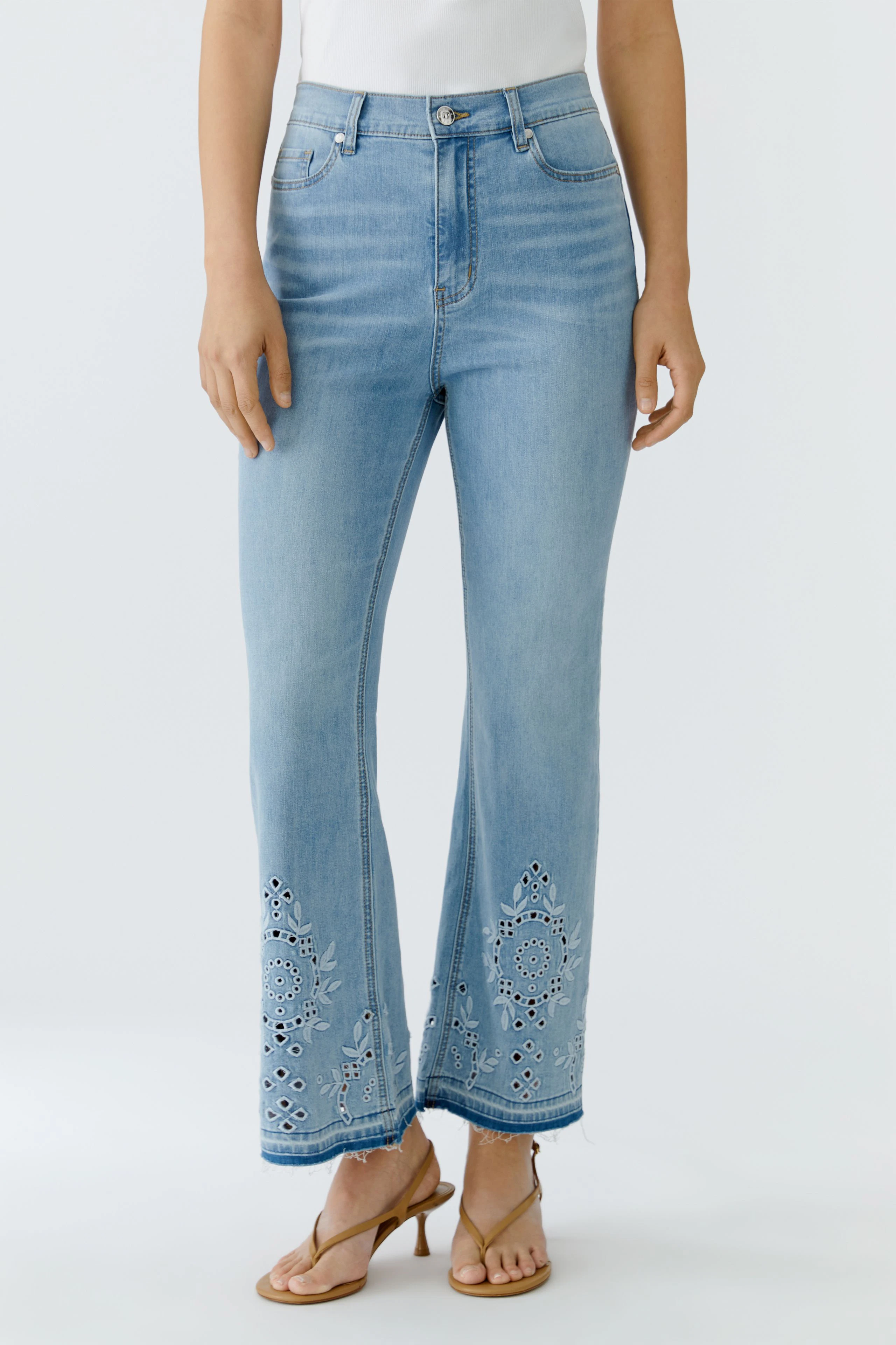 Frau in Jeans Bootcut: Hellblaue Jeans mit Stickerei am Saum, kombiniert mit weißem Top und Sandalen.