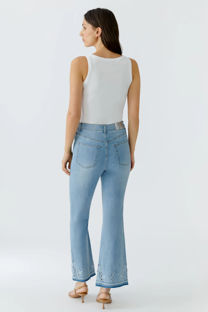 Frau in Jeans Bootcut: Weißes Top, hellblaue Jeans mit Stickerei, lässiger Look.