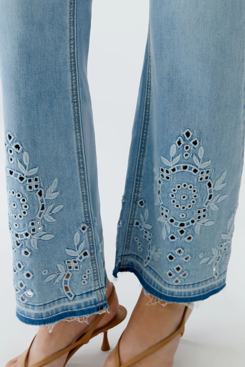 Jeans Bootcut: Detailansicht der Stickerei an den Hosenbeinen, getragen von einer Frau mit Sandalen.