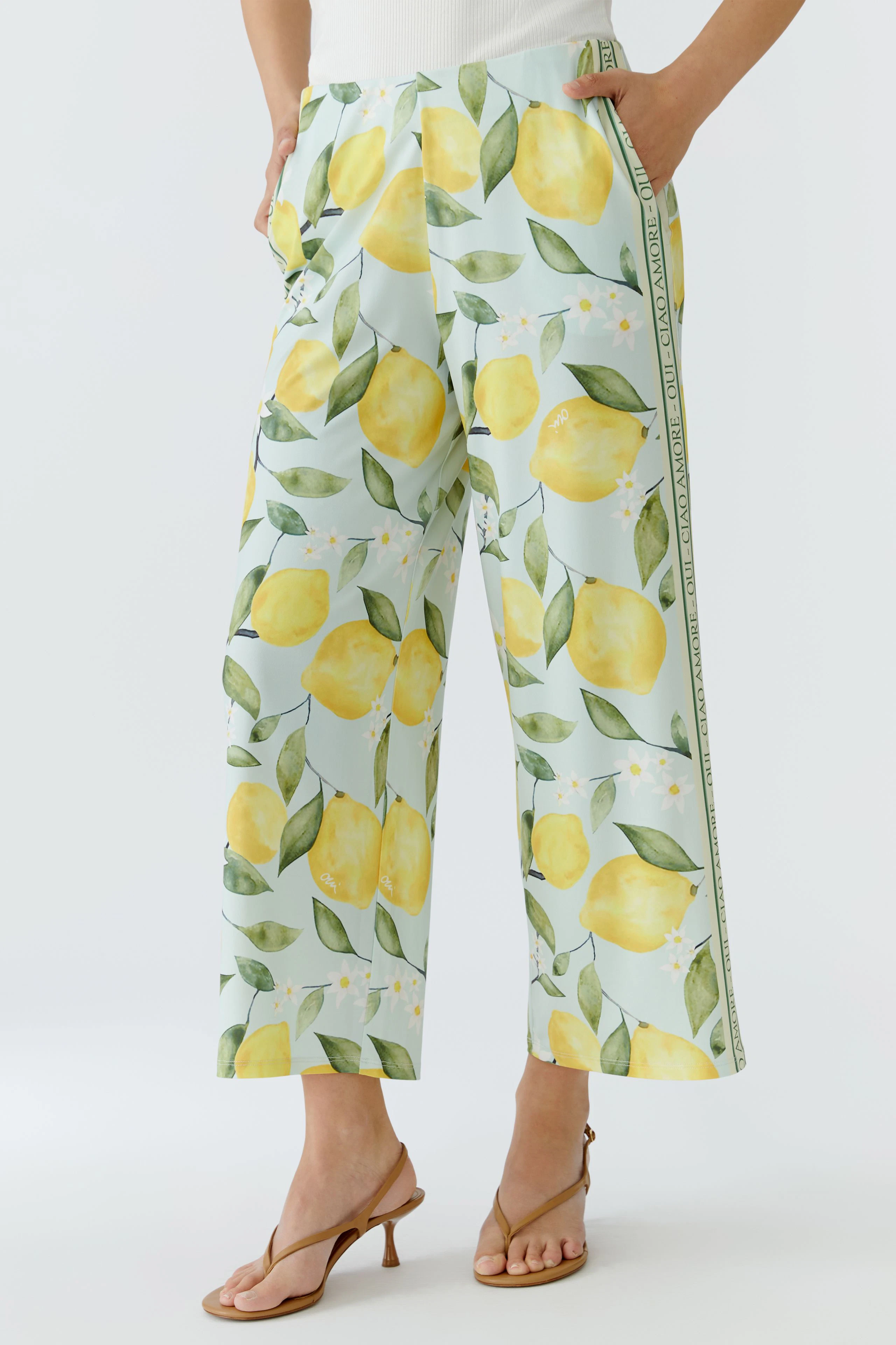 Woman in lemon-patterned culotte, standing confidently in sandals. Fresh and vibrant look.