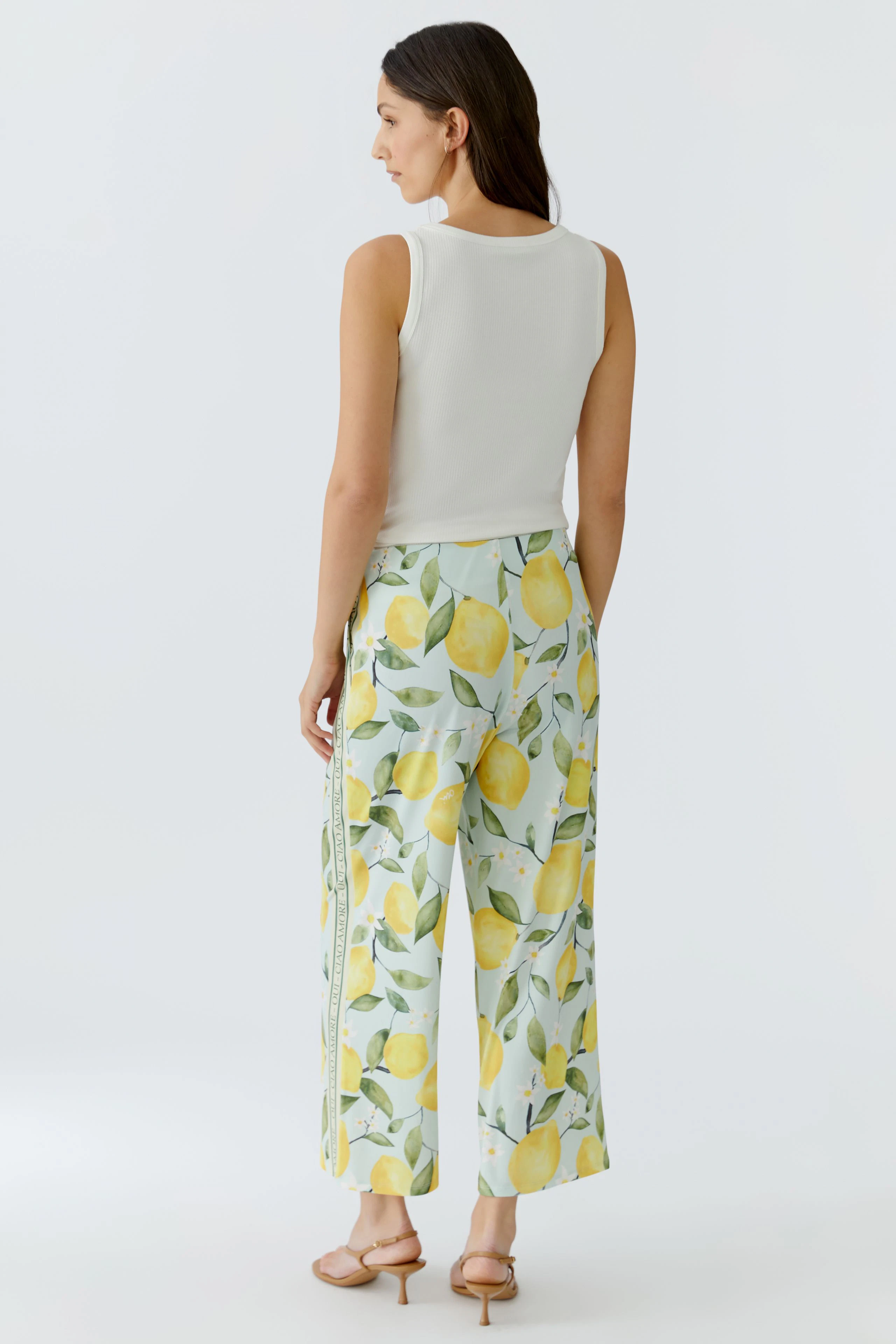 Woman in lemon-patterned culotte and white top, standing confidently. Casual and fresh look.