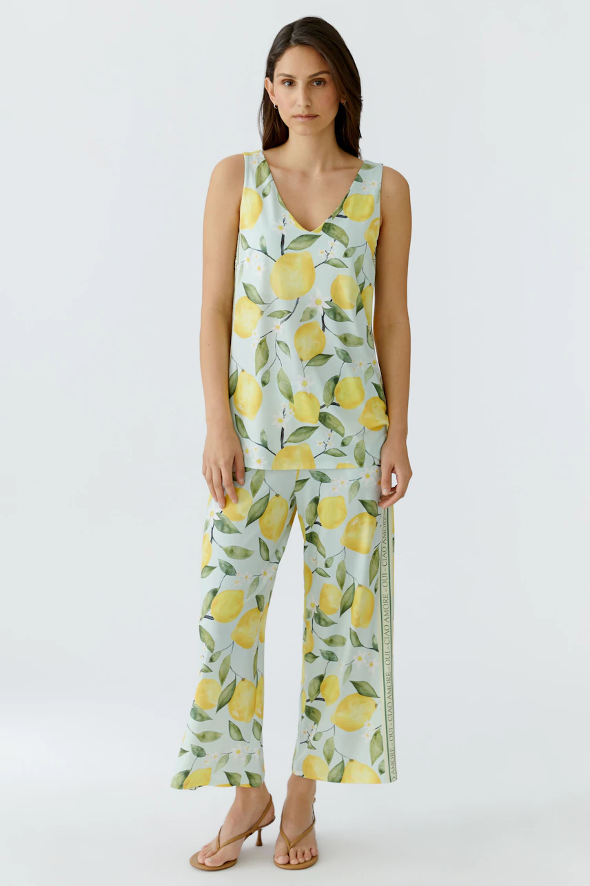 Woman in lemon-patterned culotte and matching top, standing confidently in sandals.