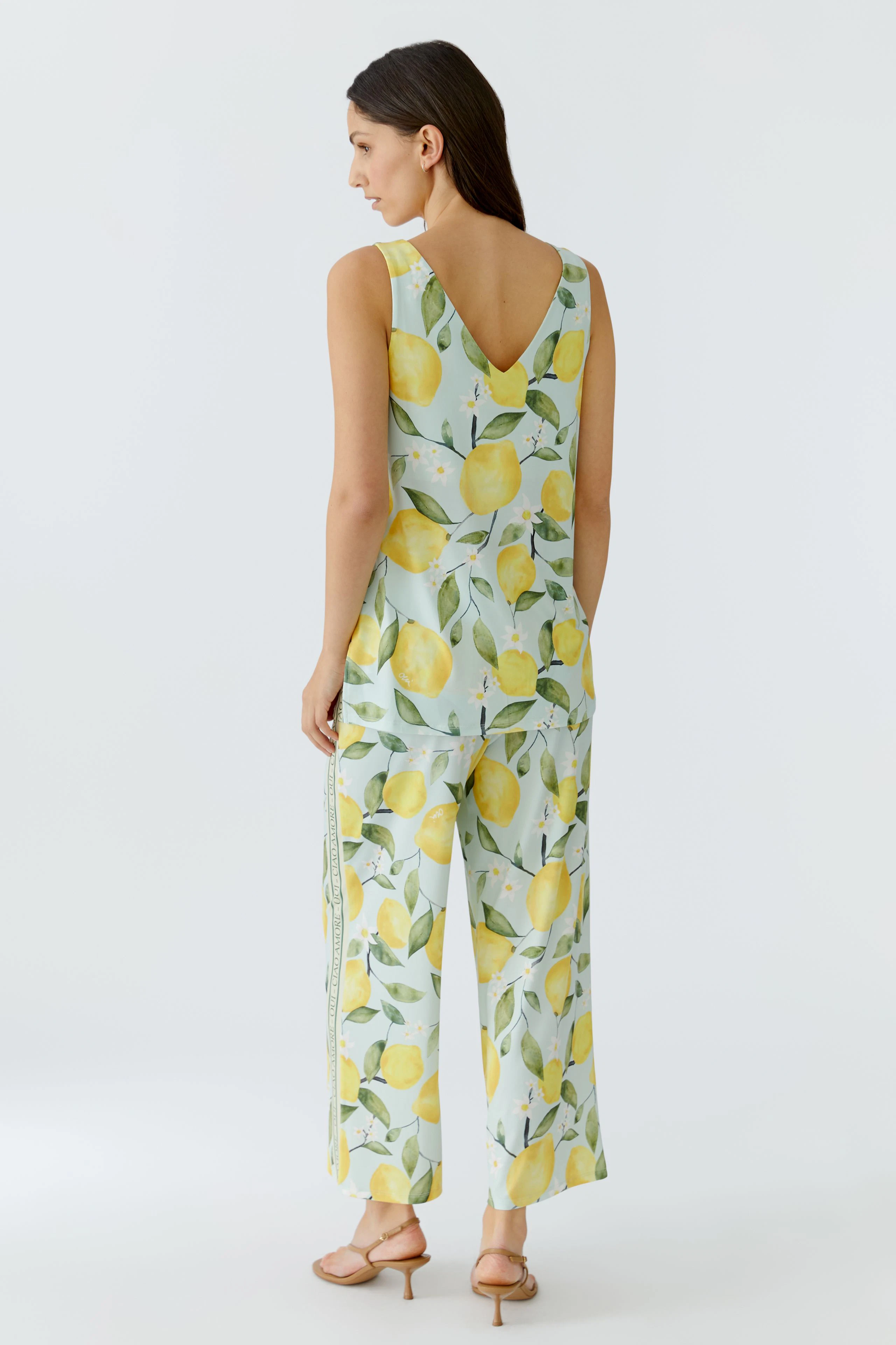 Woman in lemon-patterned top and matching pants, back view. Sleeveless design with a V-neck.