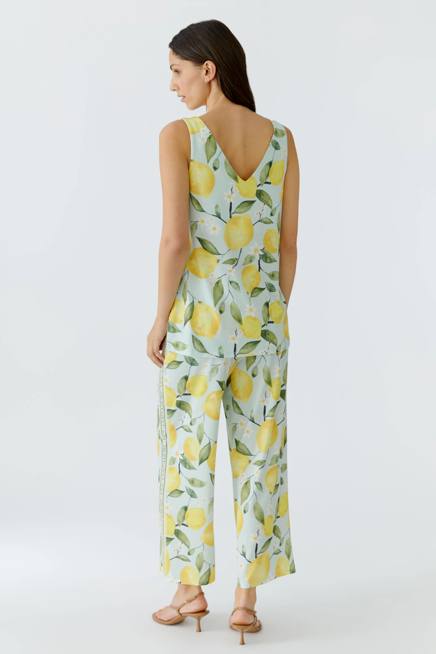 Damen-Top: Frau im ärmellosen Top mit Zitronenprint, kombiniert mit passender Hose, von hinten gezeigt.