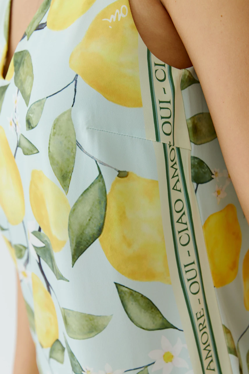 Damen-Top mit Zitronenprint: Frau trägt ärmelloses Top mit frischem Zitronenmuster und Schriftzug-Details.