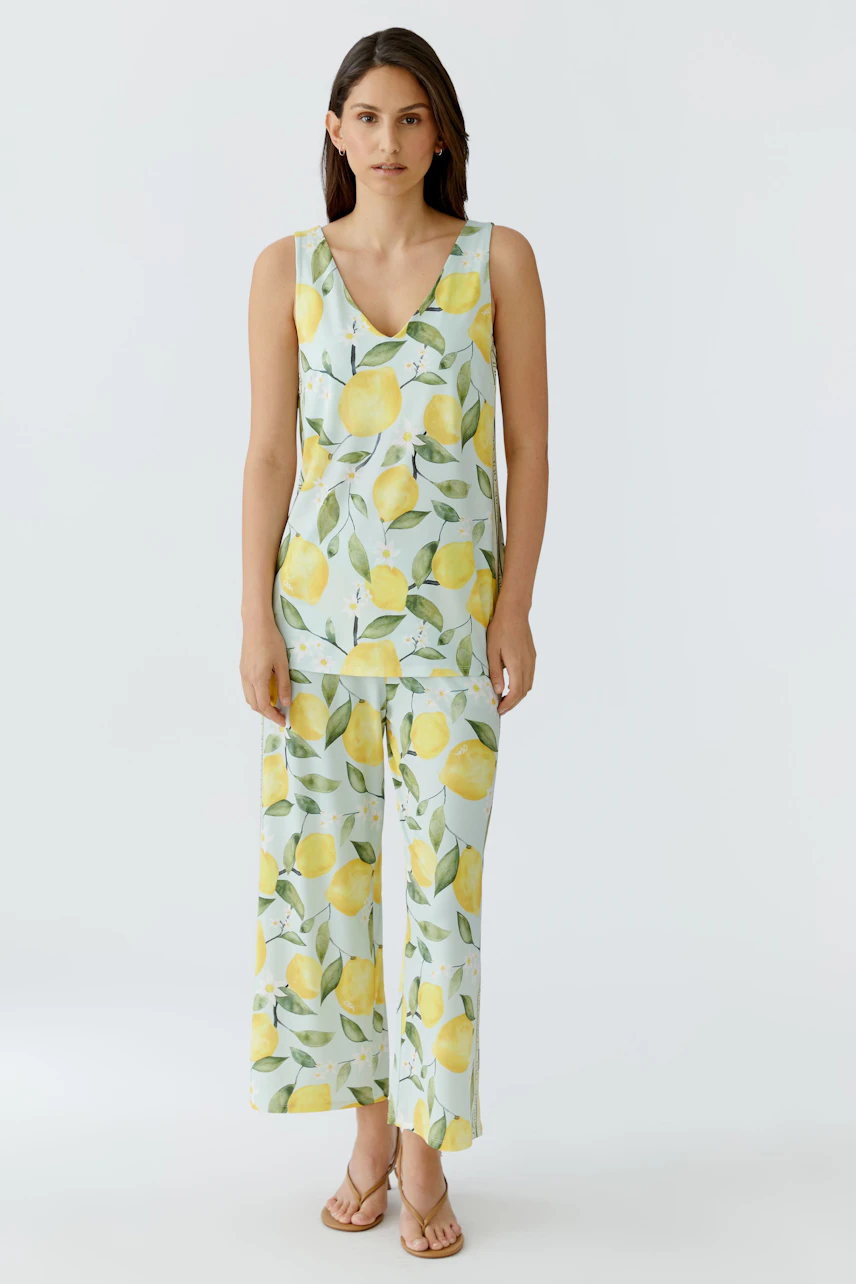 Damen-Top: Frau im ärmellosen Top mit Zitronenprint, kombiniert mit passender Hose, steht entspannt.