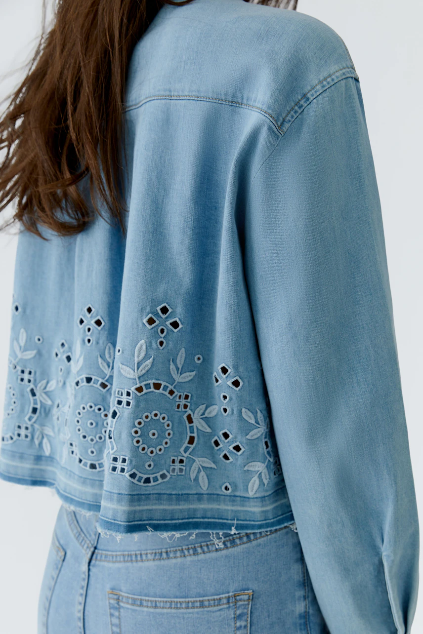 Casual denim jacket: Woman in light blue jeans jacket with intricate cut-out patterns on the back.