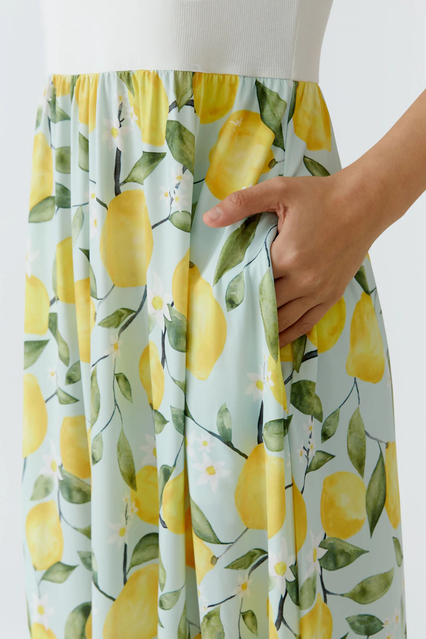 Midikleid mit Zitronenprint: Frau zeigt das Kleid mit frischem Muster und praktischer Tasche.