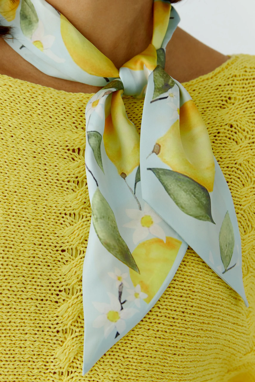 Woman in yellow knit with lemon-patterned scarf tied around neck.