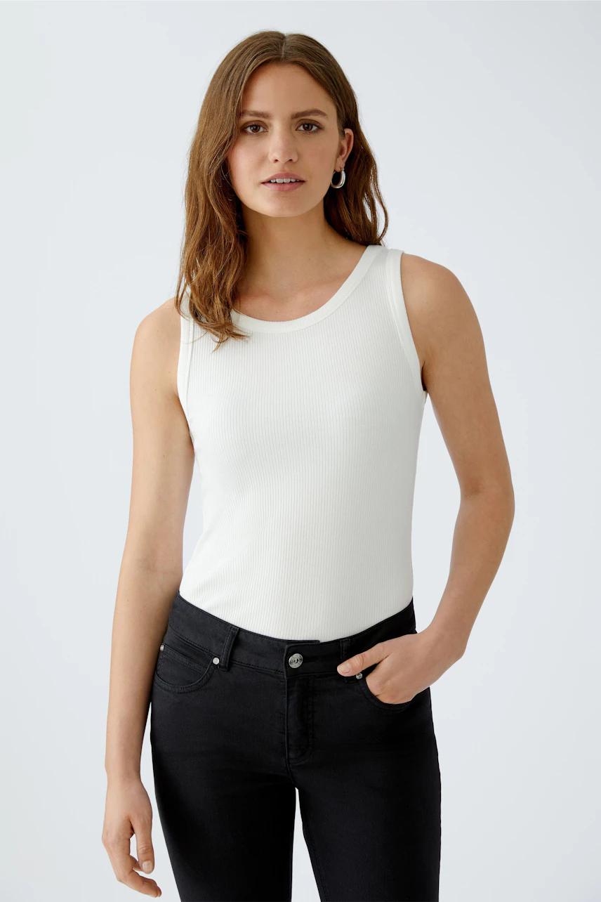 Stylish women's top: A woman in a white sleeveless top paired with black jeans, exuding confidence.