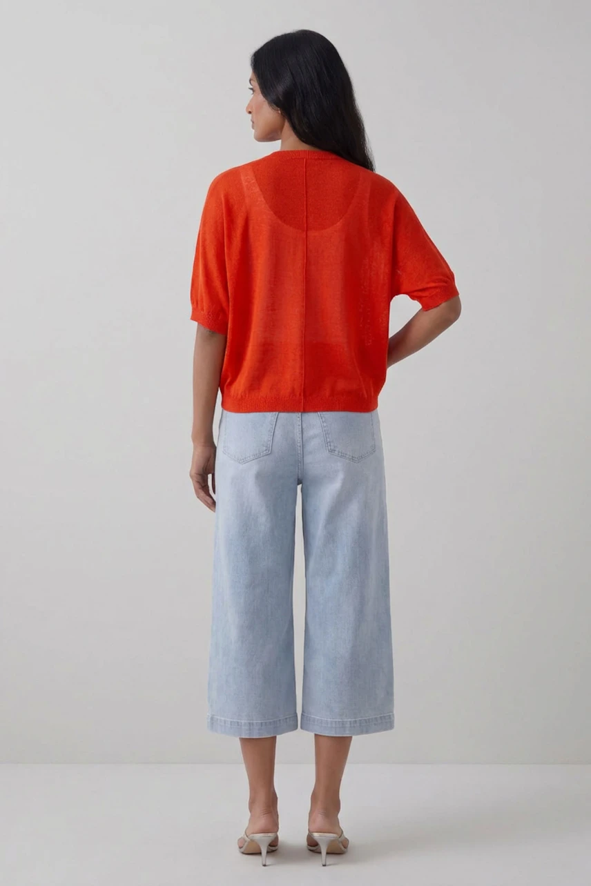 Woman in vibrant orange cardigan, paired with light blue jeans, standing confidently.