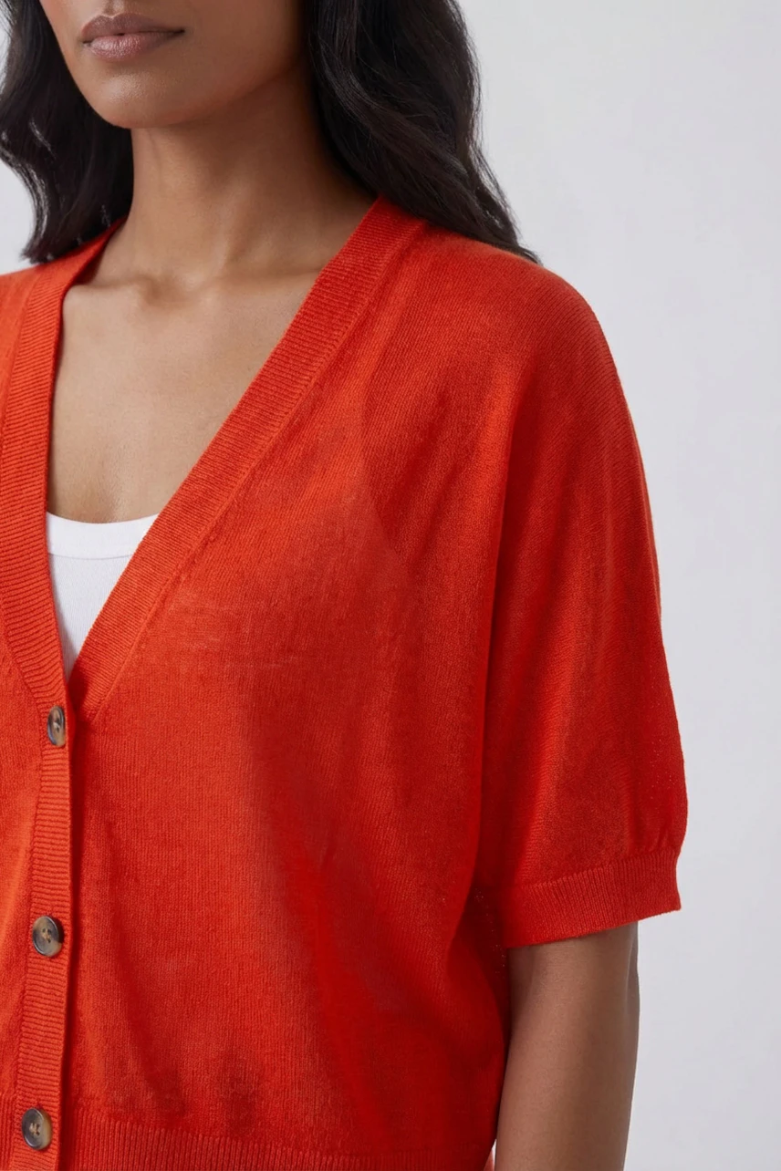 Woman in vibrant orange cardigan over white top, showcasing casual style.