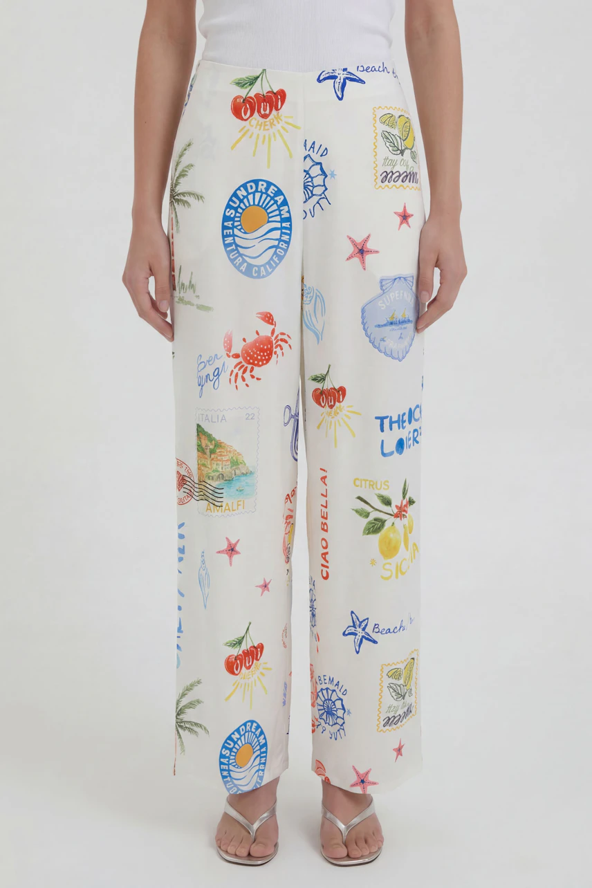 Casual Marlene pants: Woman in white printed Marlene pants with colorful beach motifs, paired with a white top.