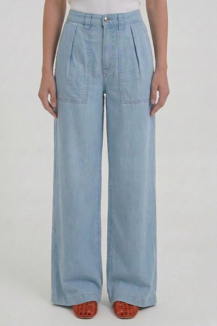 Woman in light blue wide leg jeans, high waist, paired with orange sandals, standing confidently.