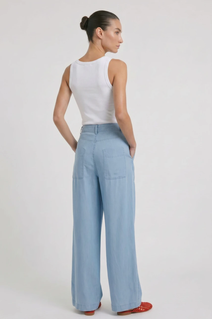 Woman in wide leg jeans and striped tank top, standing confidently. Casual and stylish look.