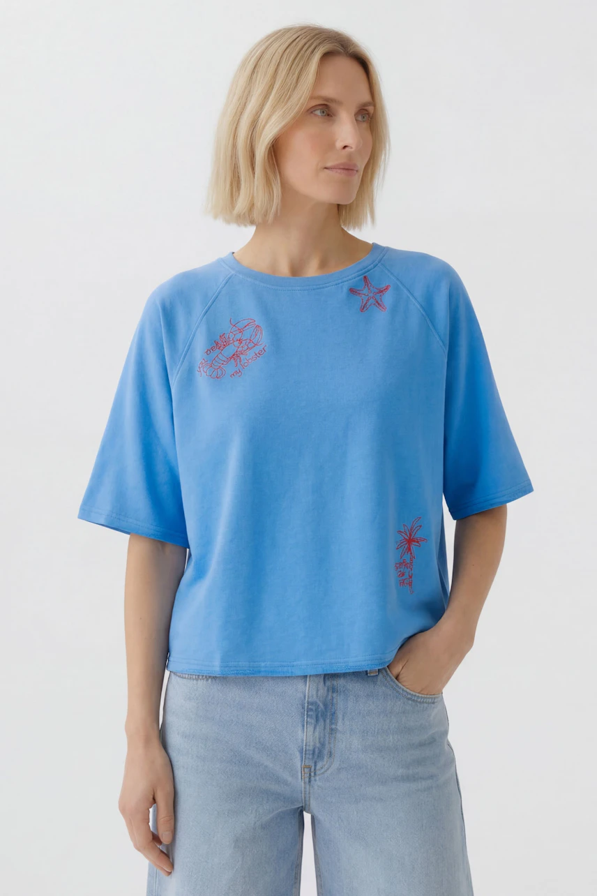 Casual women's sweatshirt: Woman in blue sweatshirt with red embroidery, short sleeves, and relaxed fit.