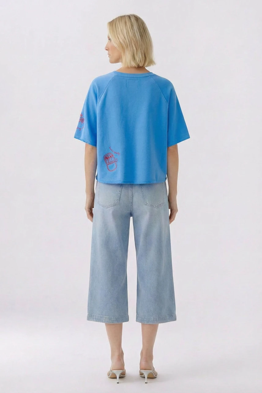 Casual women's sweatshirt: Woman in blue sweatshirt and light denim culottes, viewed from the back.