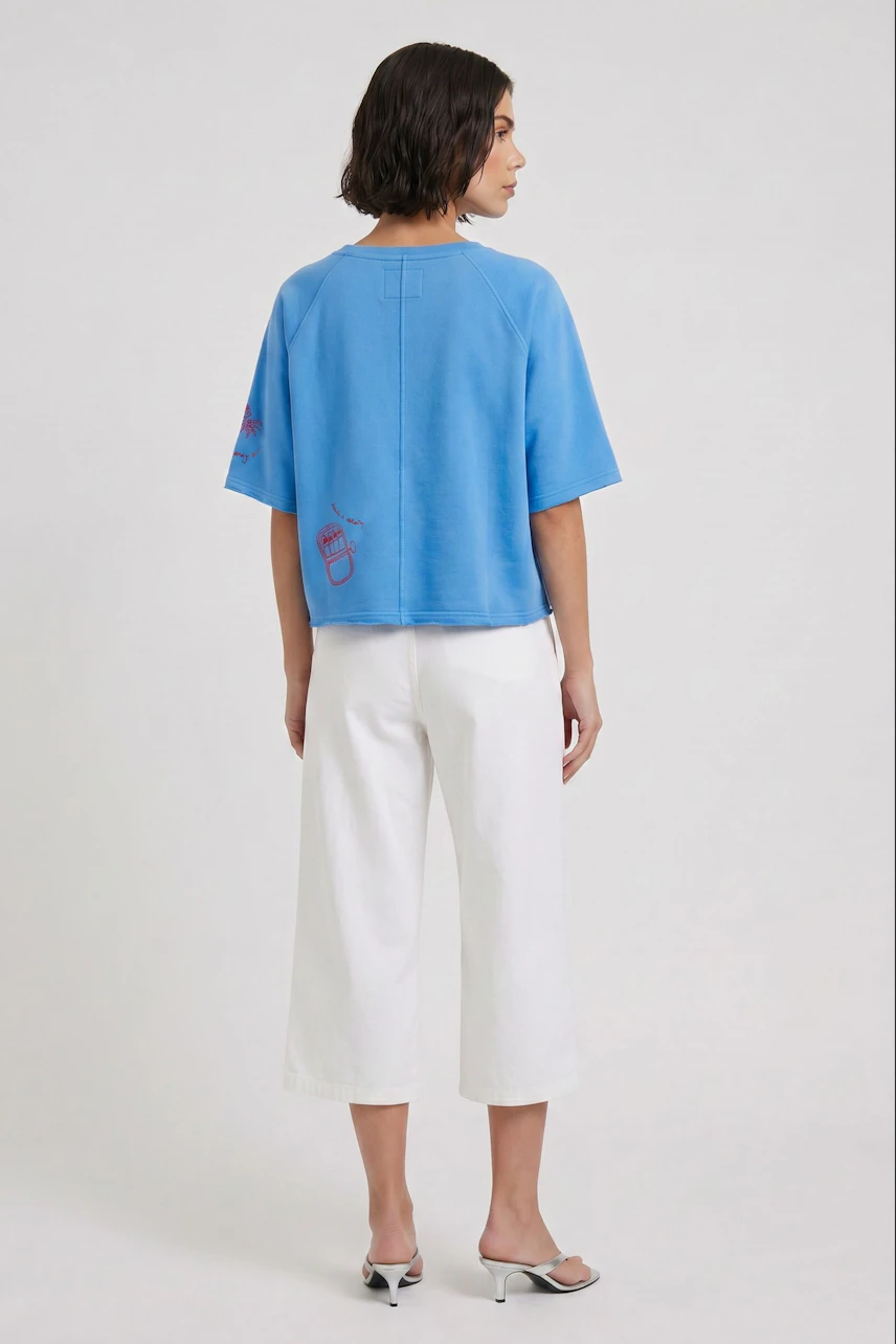 Casual women's sweatshirt: Woman in blue sweatshirt and light denim culottes, viewed from the back.