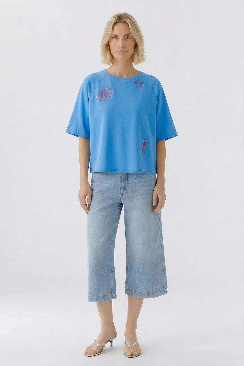 Casual women's sweatshirt: Woman in blue sweatshirt with subtle prints, paired with wide-leg jeans and sandals.