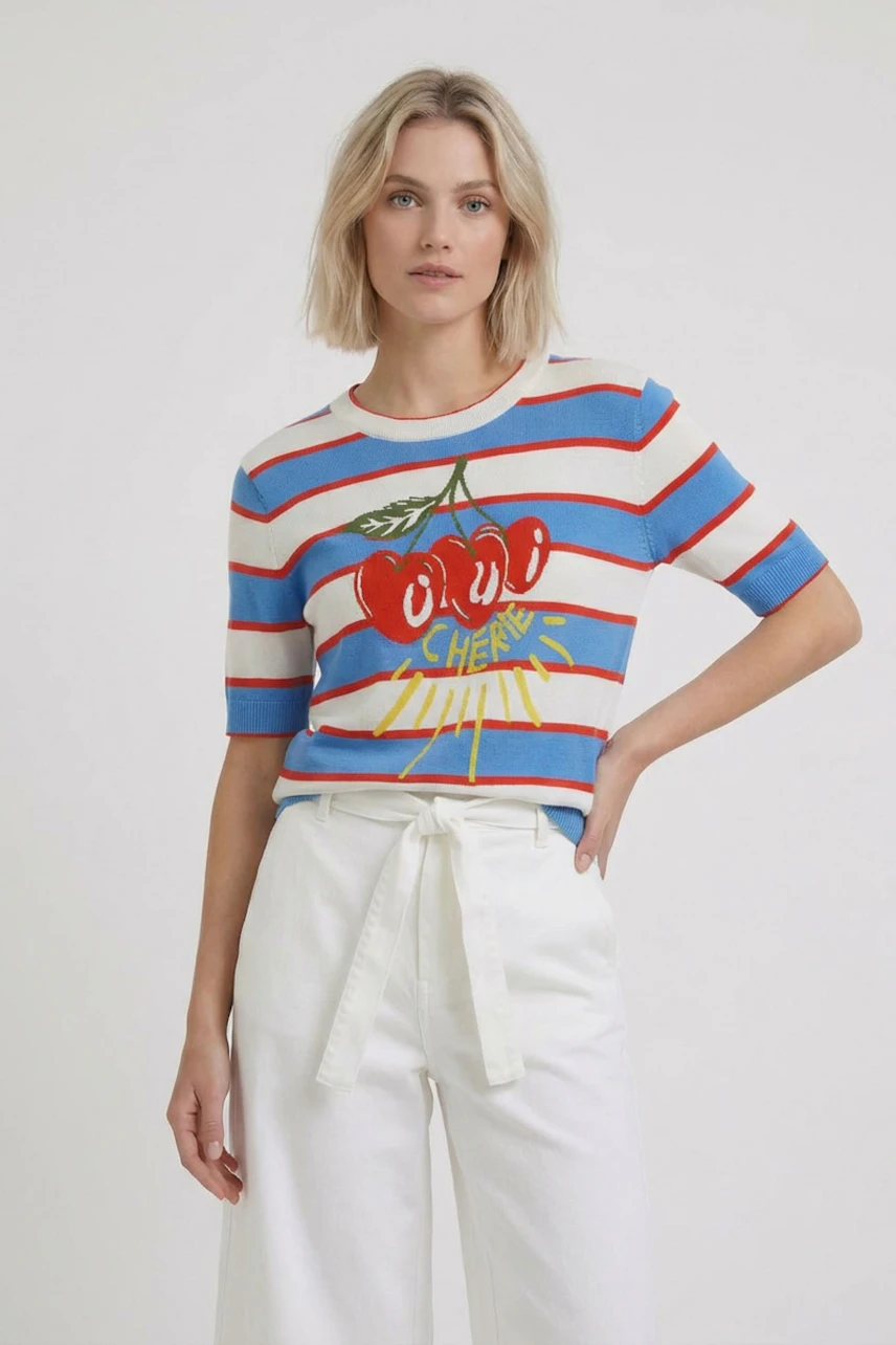 Casual women's pullover: Woman in striped pullover with cherry print, paired with white pants, looks relaxed.