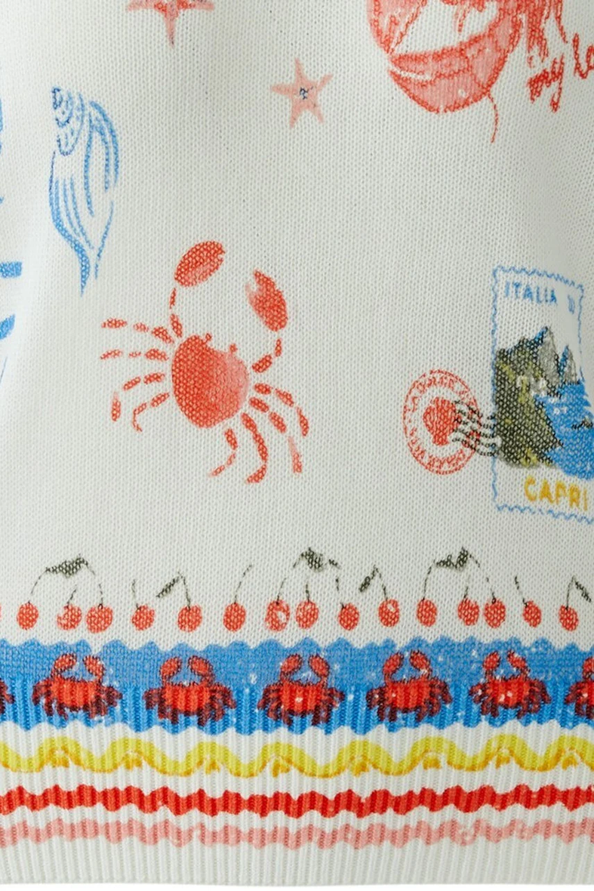 White pullover with colorful embroidery, including a lobster and lemons, on a flat surface.