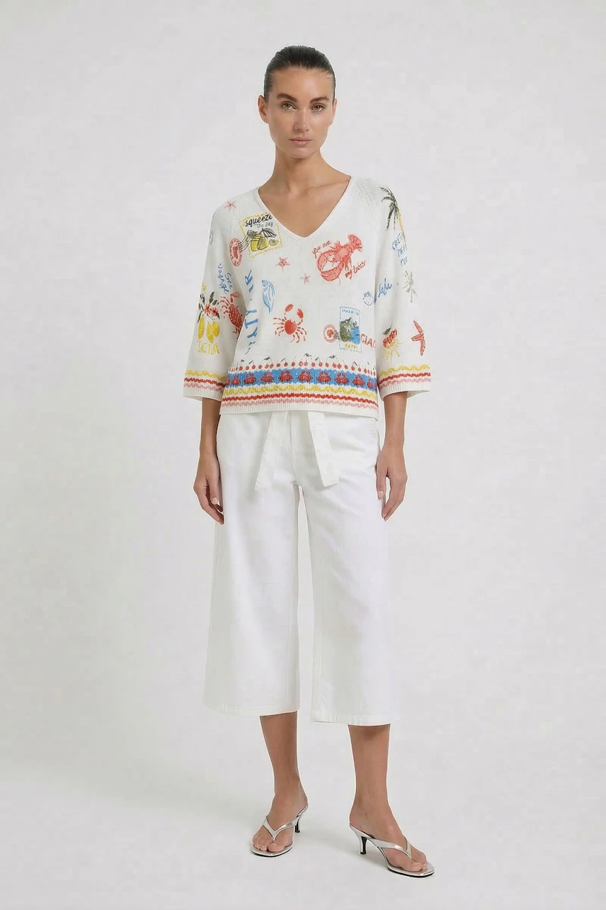 Casual women's pullover: Woman in a colorful V-neck pullover with white pants and sandals, standing confidently.