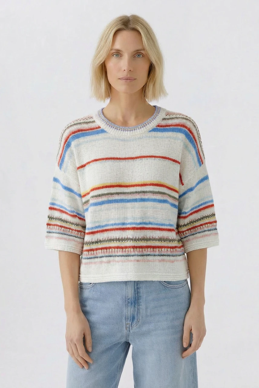 Casual women's pullover: Woman in a colorful striped pullover with light blue jeans, standing confidently.