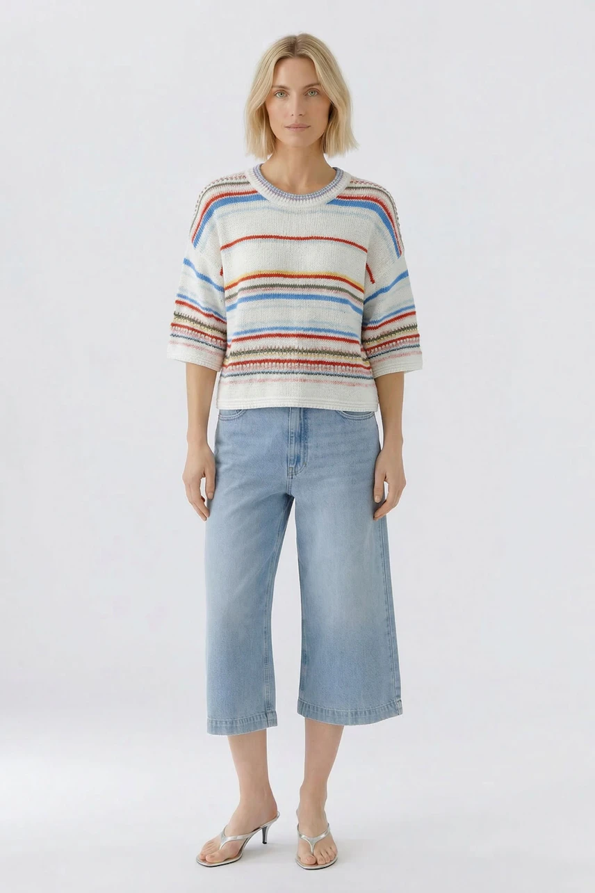 Casual pullover: Woman in a striped pullover with wide sleeves and light blue cropped jeans stands confidently.