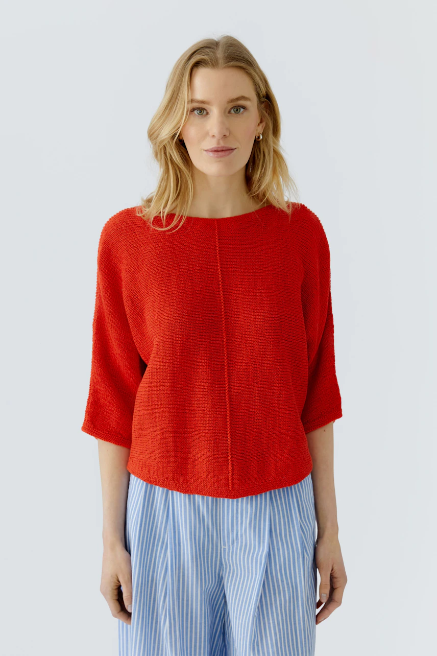 Roter Damen-Pullover: Frau im lockeren Pullover mit halblangen Ärmeln und blauer gestreifter Hose.