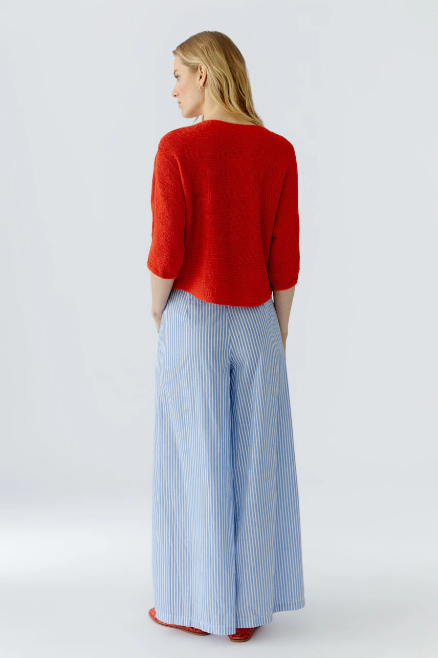 Frau im roten Pullover, kombiniert mit hellblauer, gestreifter Hose. Lässiger Look, ideal für den Alltag.