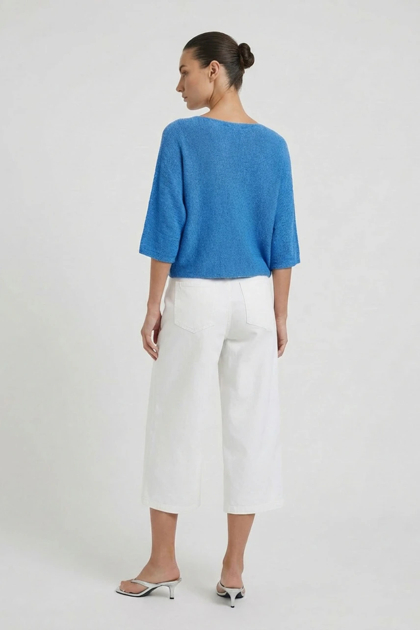 Frau im blauen Pullover und weißen Hosen, seitlich stehend. Lässiger Look für den Alltag.