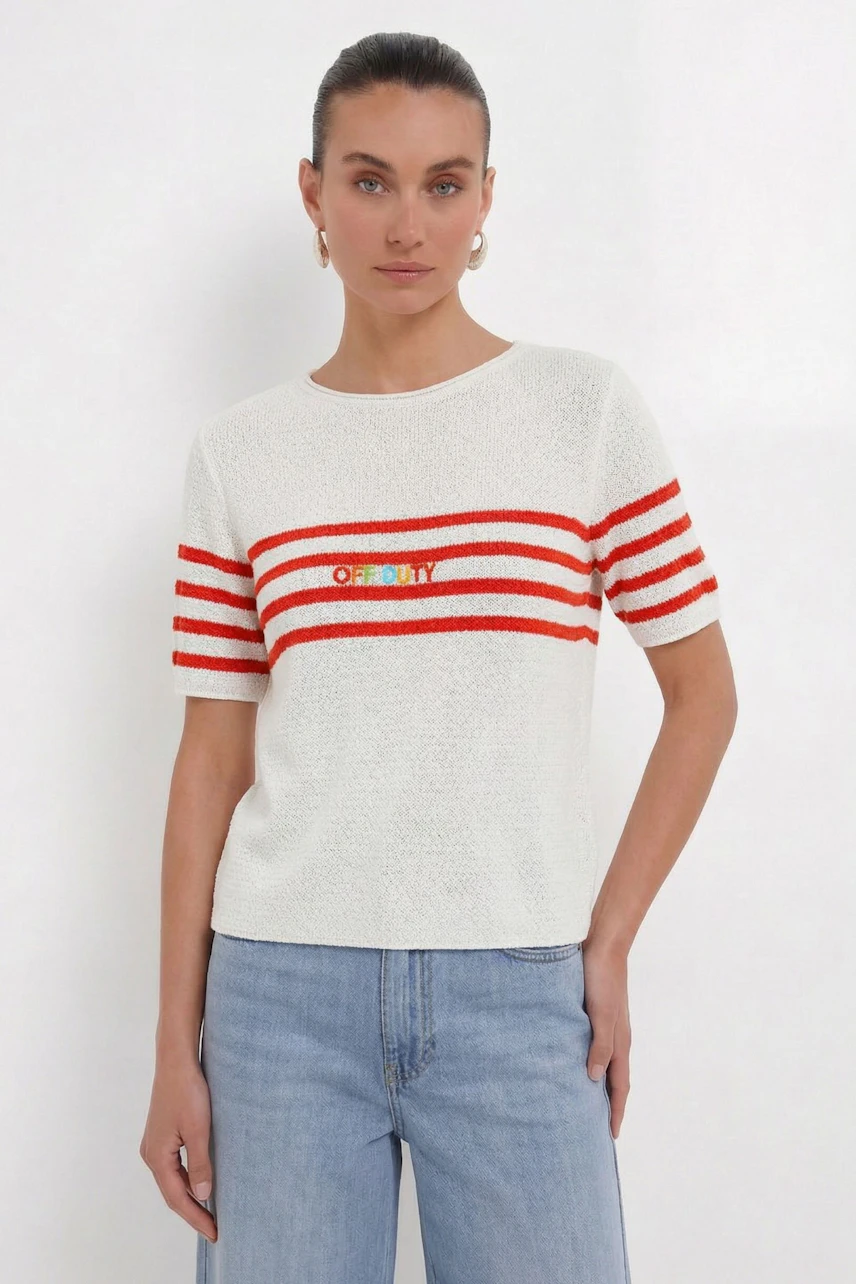 Damen-Pullover: Frau im weißen Pullover mit roten Streifen und Schriftzug, kombiniert mit blauen Jeans.