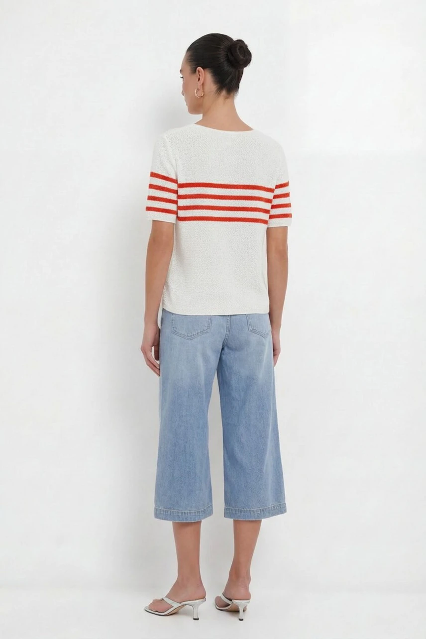 Lässiger Damen-Pullover: Frau im weißen Pullover mit roten Streifen und blauen Jeans-Culottes von hinten.