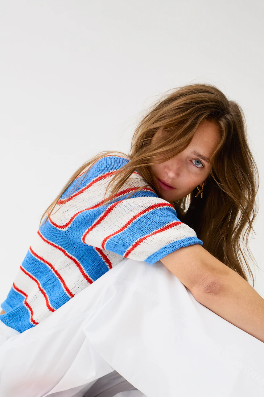 Casual pullover: Woman in a striped blue, red, and white pullover with relaxed white pants.