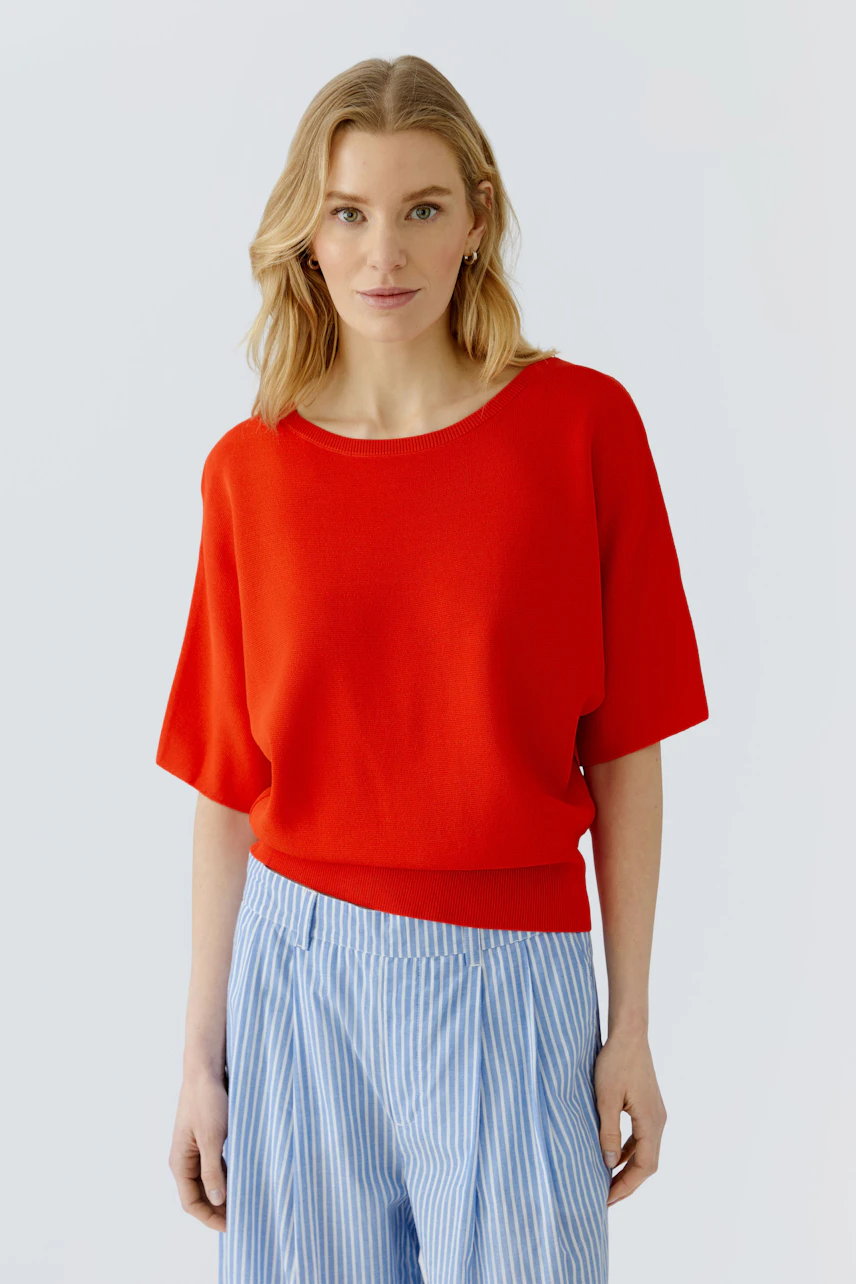 Casual women's pullover: Woman in a red pullover with 3/4 sleeves and light blue striped pants.