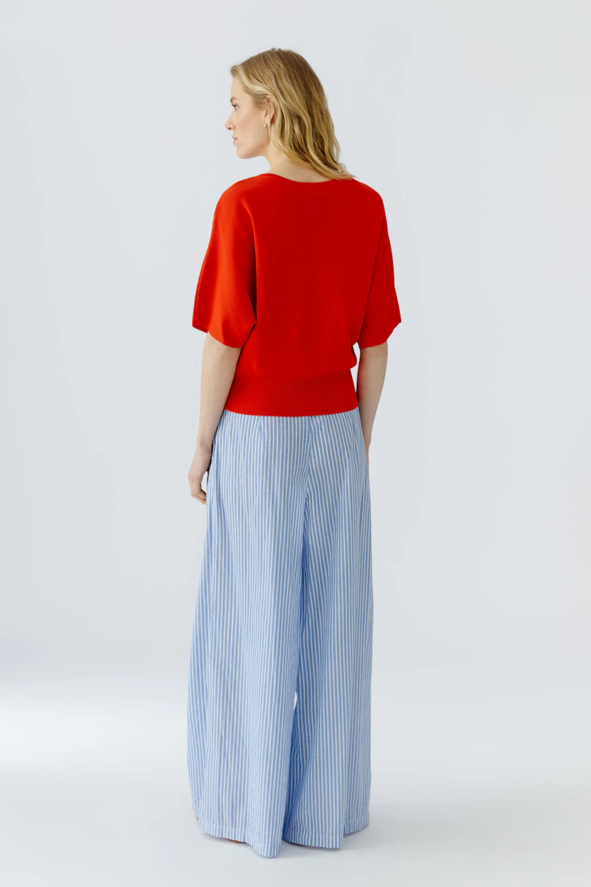 Casual women's pullover: Woman in a vibrant red pullover with wide blue pants, standing confidently.