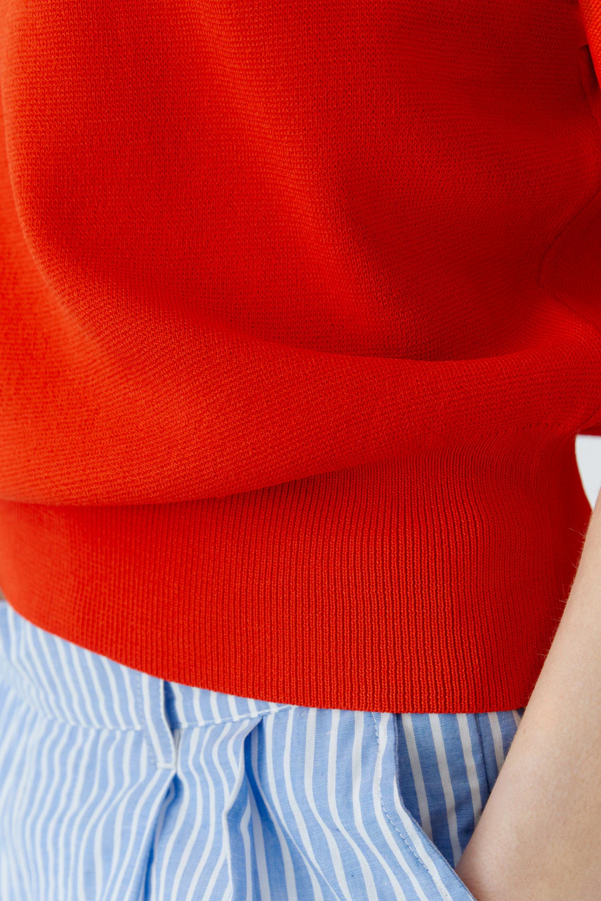 Casual women's pullover: Woman in a red pullover with 3/4 sleeves and blue striped pants, looking poised.