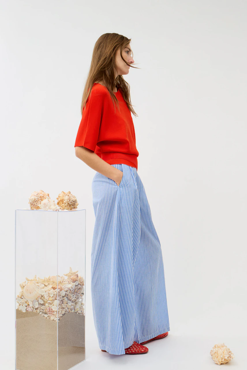 Woman in a red pullover with short sleeves, paired with blue striped wide-leg pants, standing confidently.