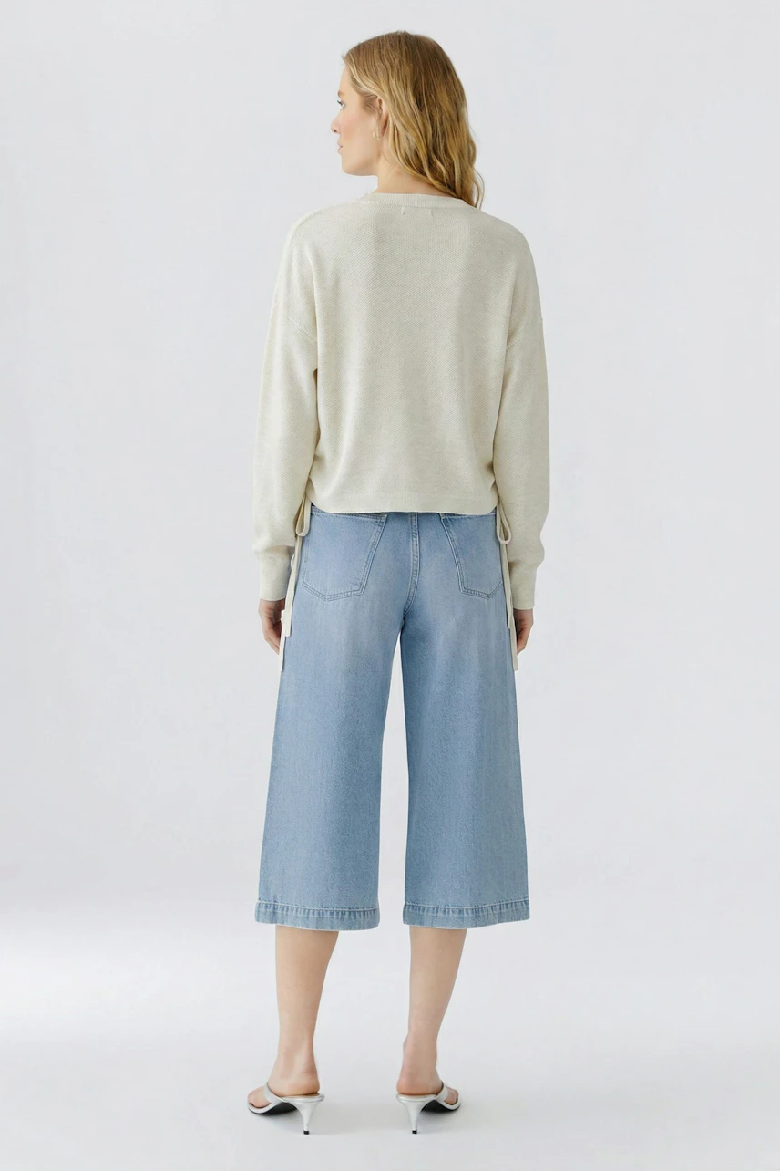 Lässiger Damen-Pullover: Frau im cremefarbenen Pullover und hellblauer Jeans, seitlich stehend.