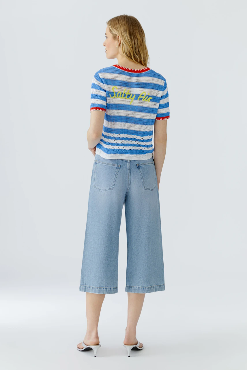 Casual cardigan: Woman in a striped cardigan with red accents, paired with light blue culottes, facing away.