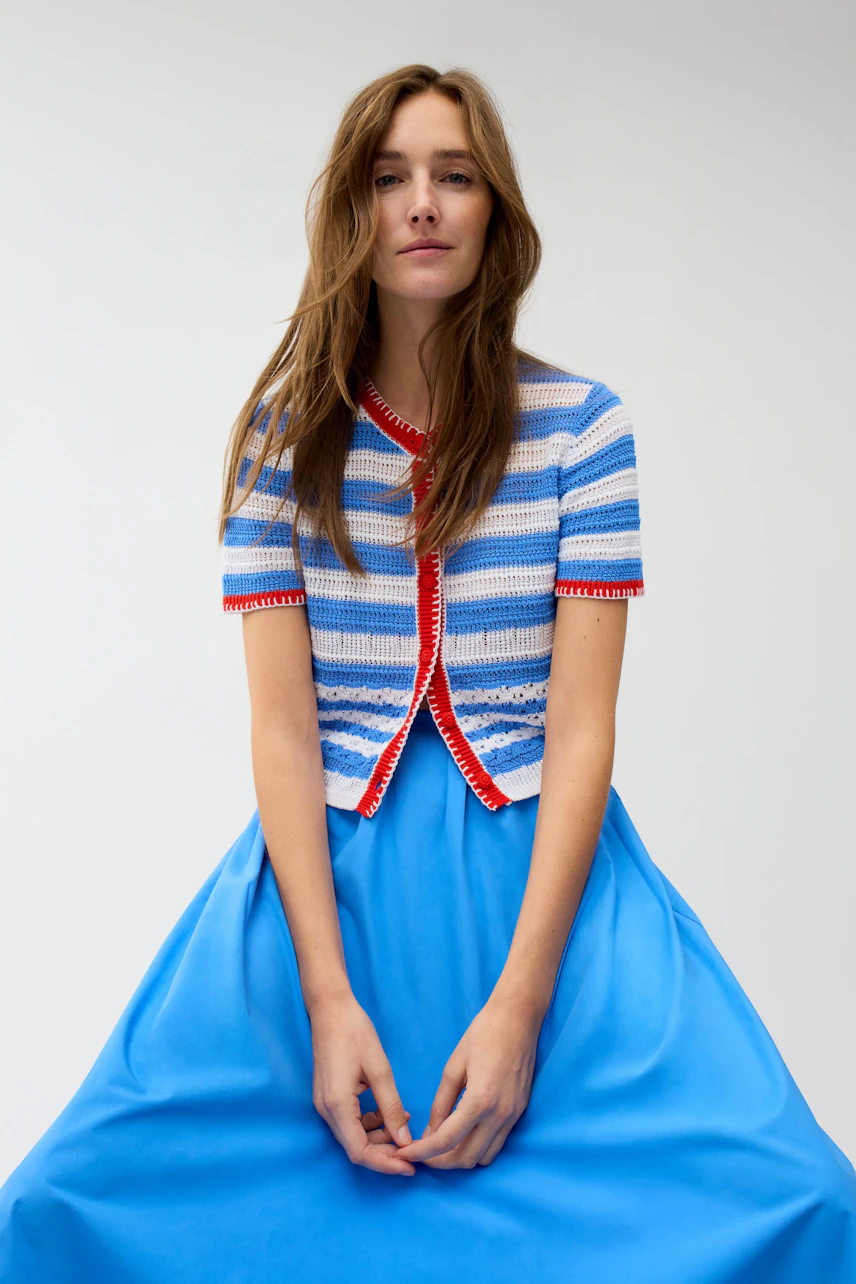 Striped cardigan: Woman in a blue and white striped cardigan with red trim, paired with a blue dress.