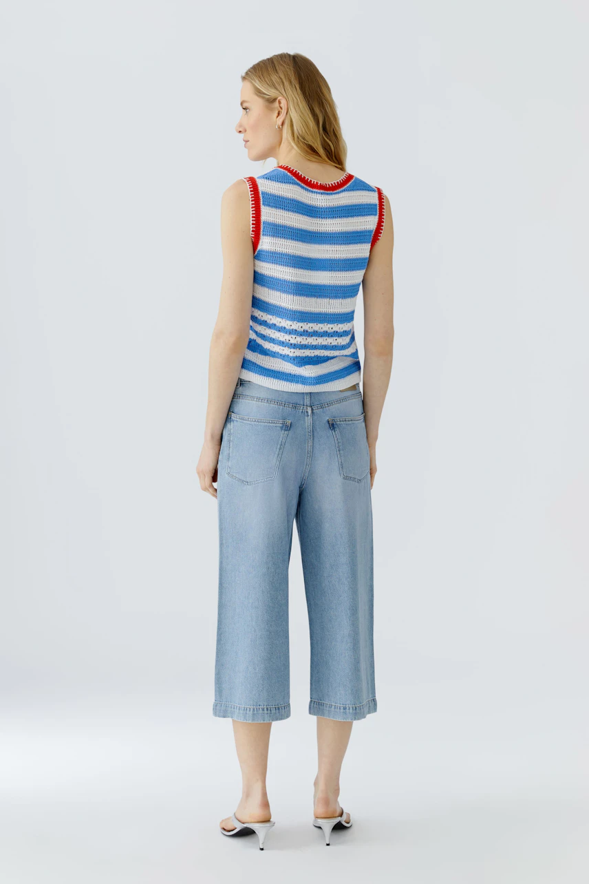 Striped top: Woman in a sleeveless blue and white striped top with red accents, paired with cropped jeans.