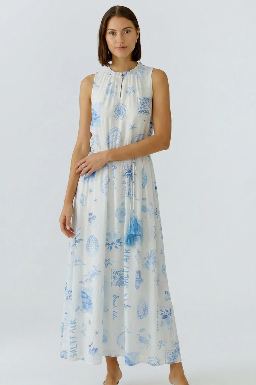 Woman in a sleeveless maxi dress with blue prints, standing confidently.