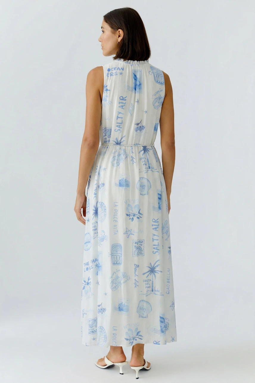 Woman in printed maxi dress with blue motifs, sleeveless design, and relaxed fit, facing away.