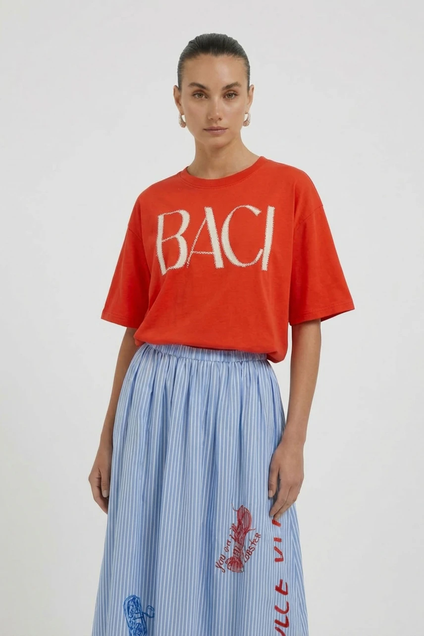 Casual women's T-shirt: Woman in red T-shirt with 'BACI' print, paired with a blue striped skirt.