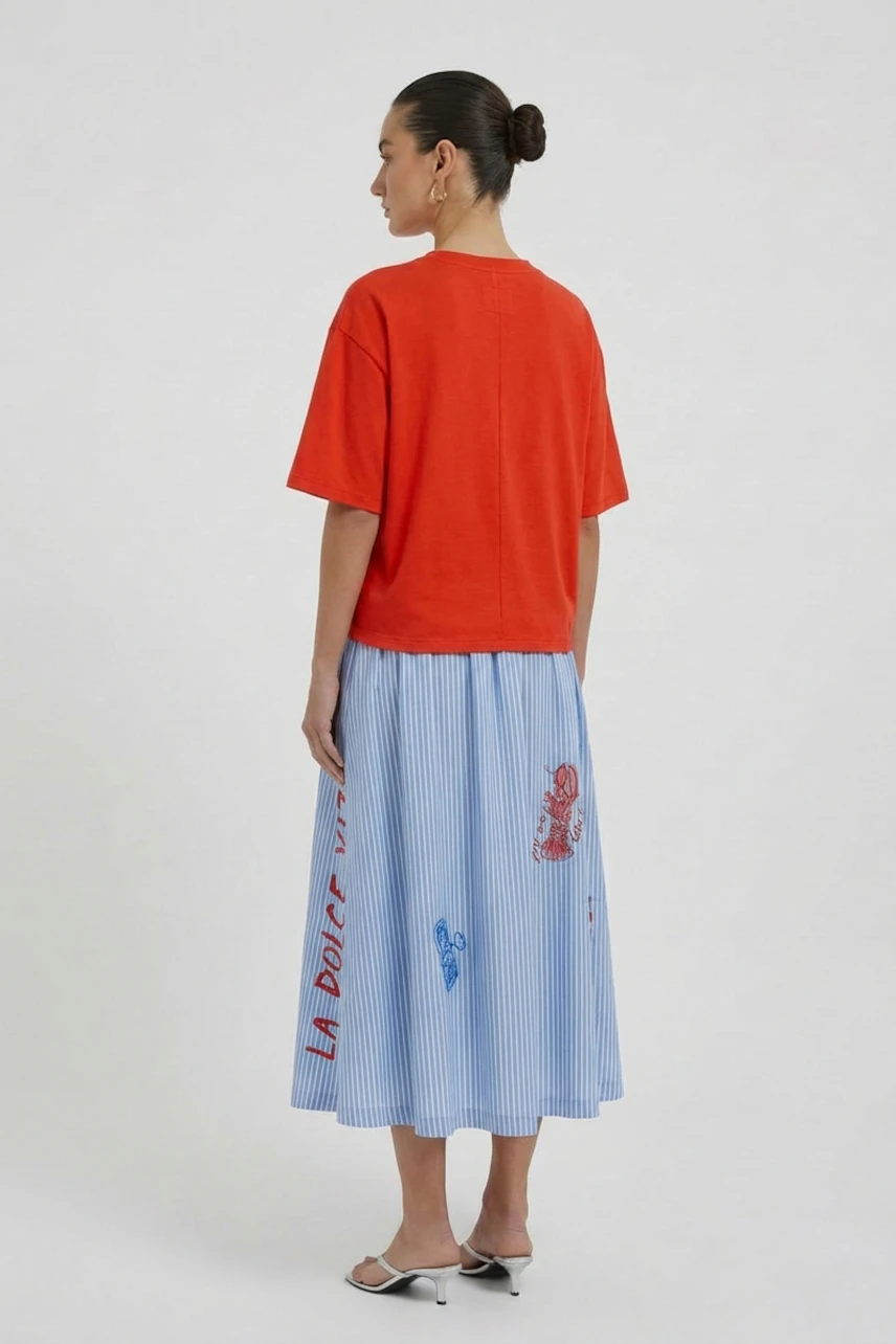 Casual women's T-shirt: Woman in a red T-shirt and blue skirt, standing with a confident posture.
