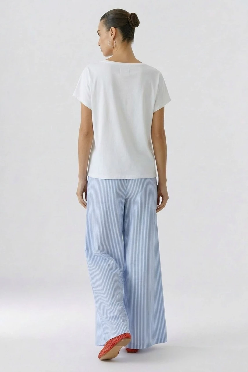 Casual women's T-shirt: Woman in a white T-shirt and striped blue pants, viewed from the back.